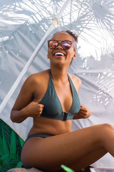 Joyful woman lounging under a beach umbrella in swimwear, exuding summer vibes.