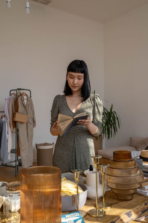 Free An Asian woman in a green dress reads a book in a stylish indoor setting with natural light. Stock Photo