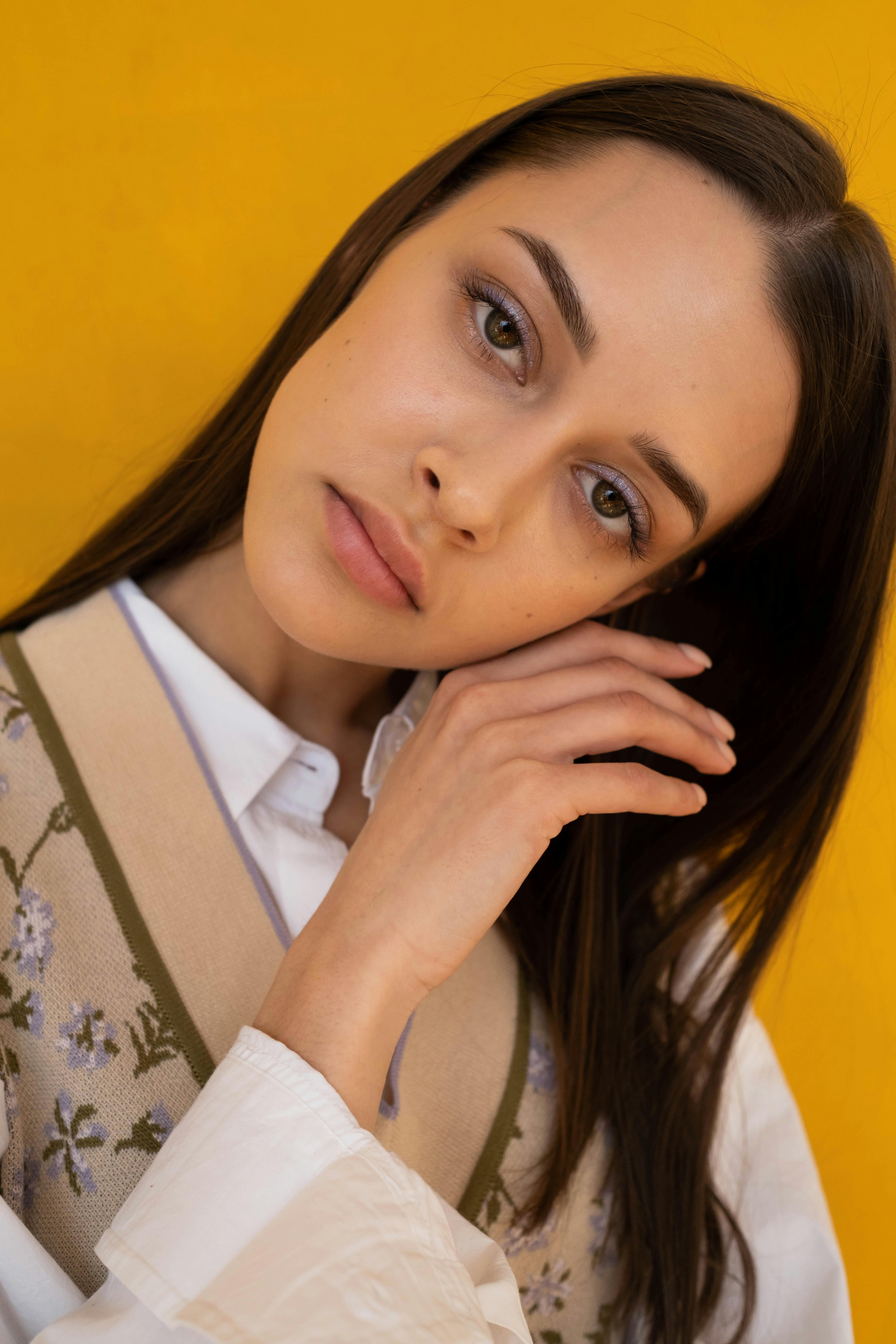 A captivating portrait of an adult woman with long brunette hair, posing against a vibrant yellow background.