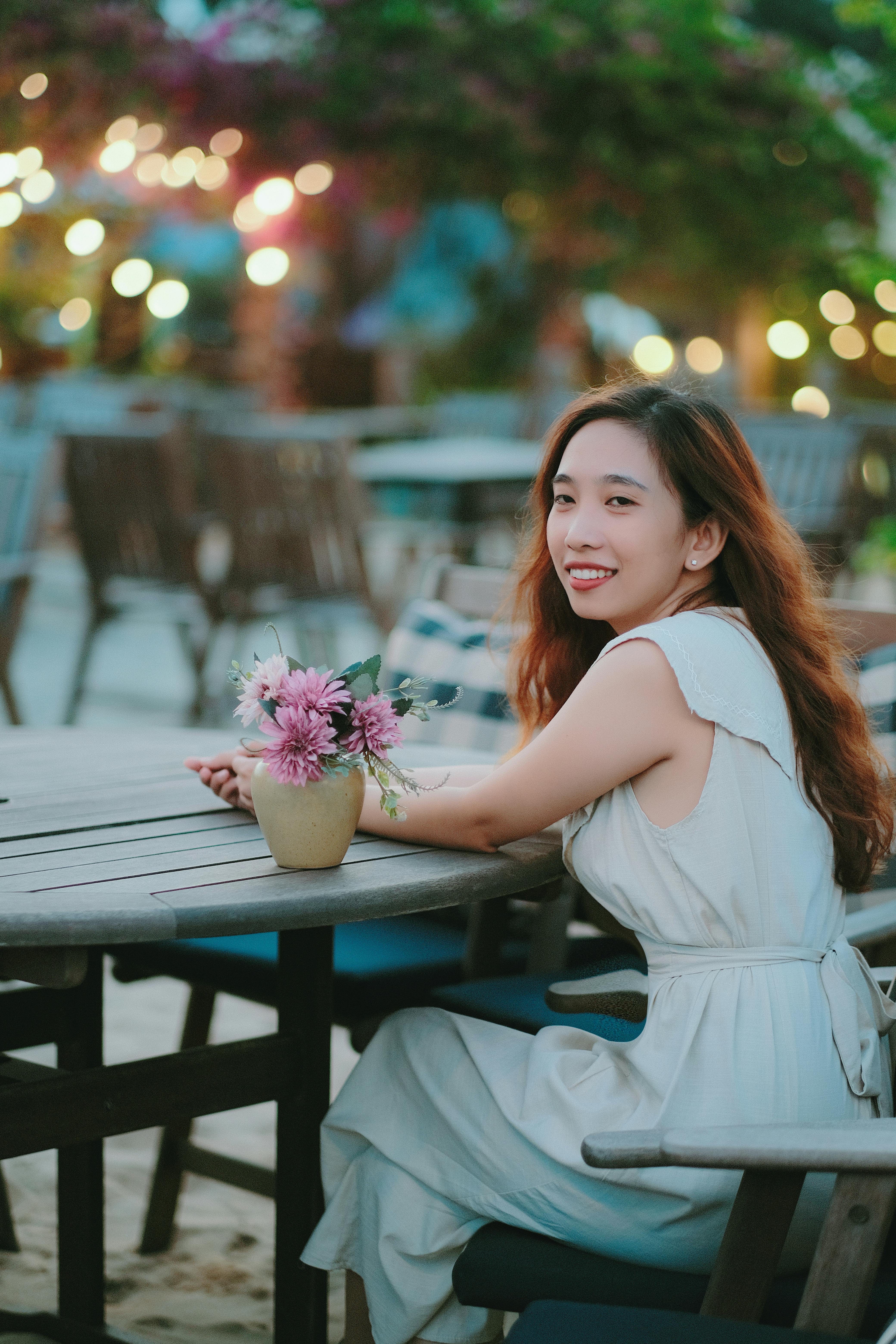 A joyful woman sitting at an outdoor cafe during the evening, surrounded by lights.