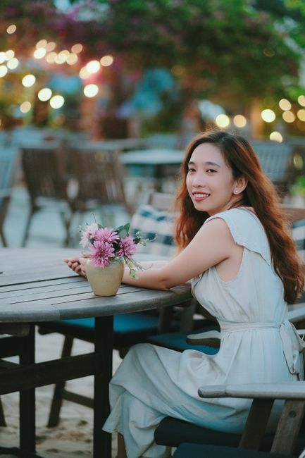 A joyful woman sitting at an outdoor cafe during the evening, surrounded by lights.