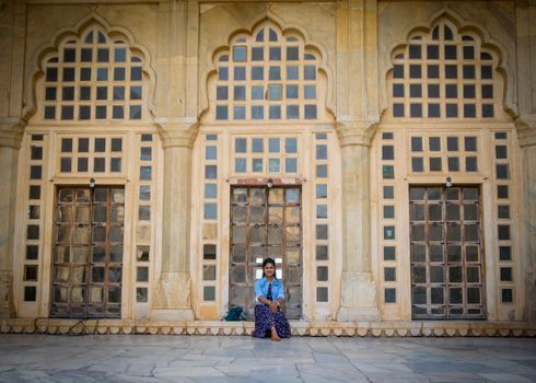 Woman sitting by ornate doors in Udaipur. Captures Rajasthani architectural beauty.