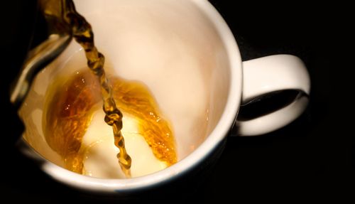 Free Close-up of hot tea being poured into a white cup, capturing the vibrant liquid and elegant flow. Stock Photo