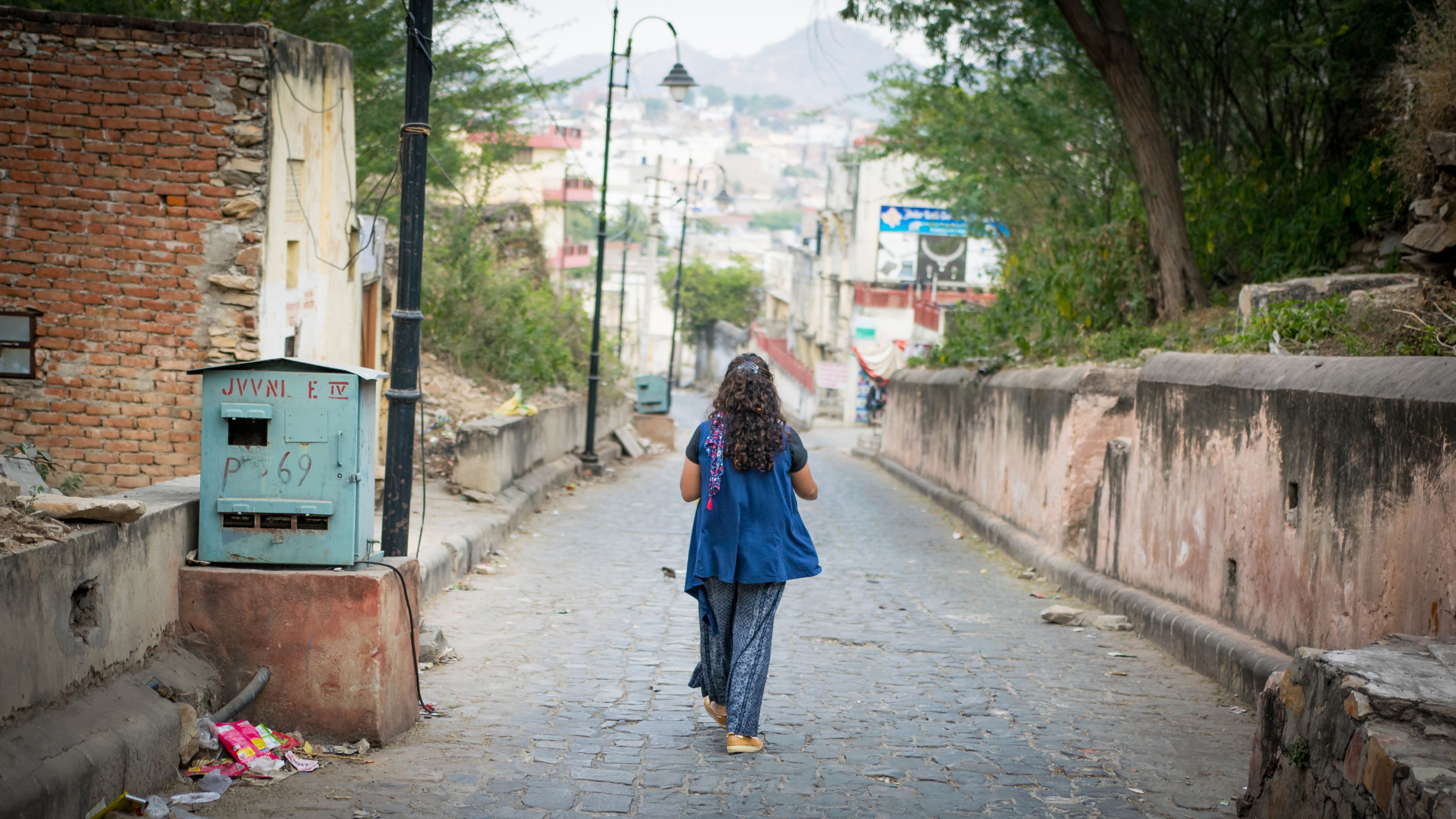 A woman strolls down a cobblestone alley in Pushkar, India, surrounded by rustic architecture.