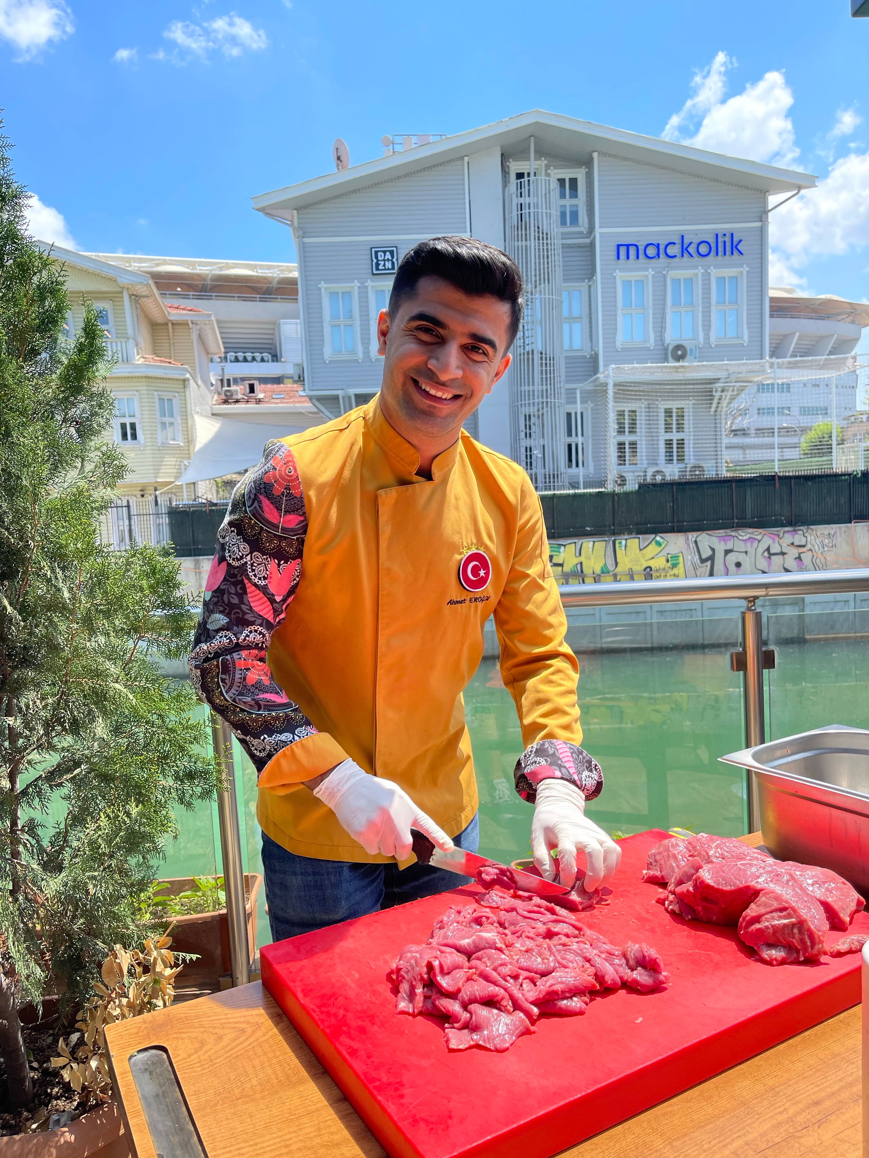 A cheerful chef preparing meat outdoors on a sunny day, showcasing culinary skills with precision.