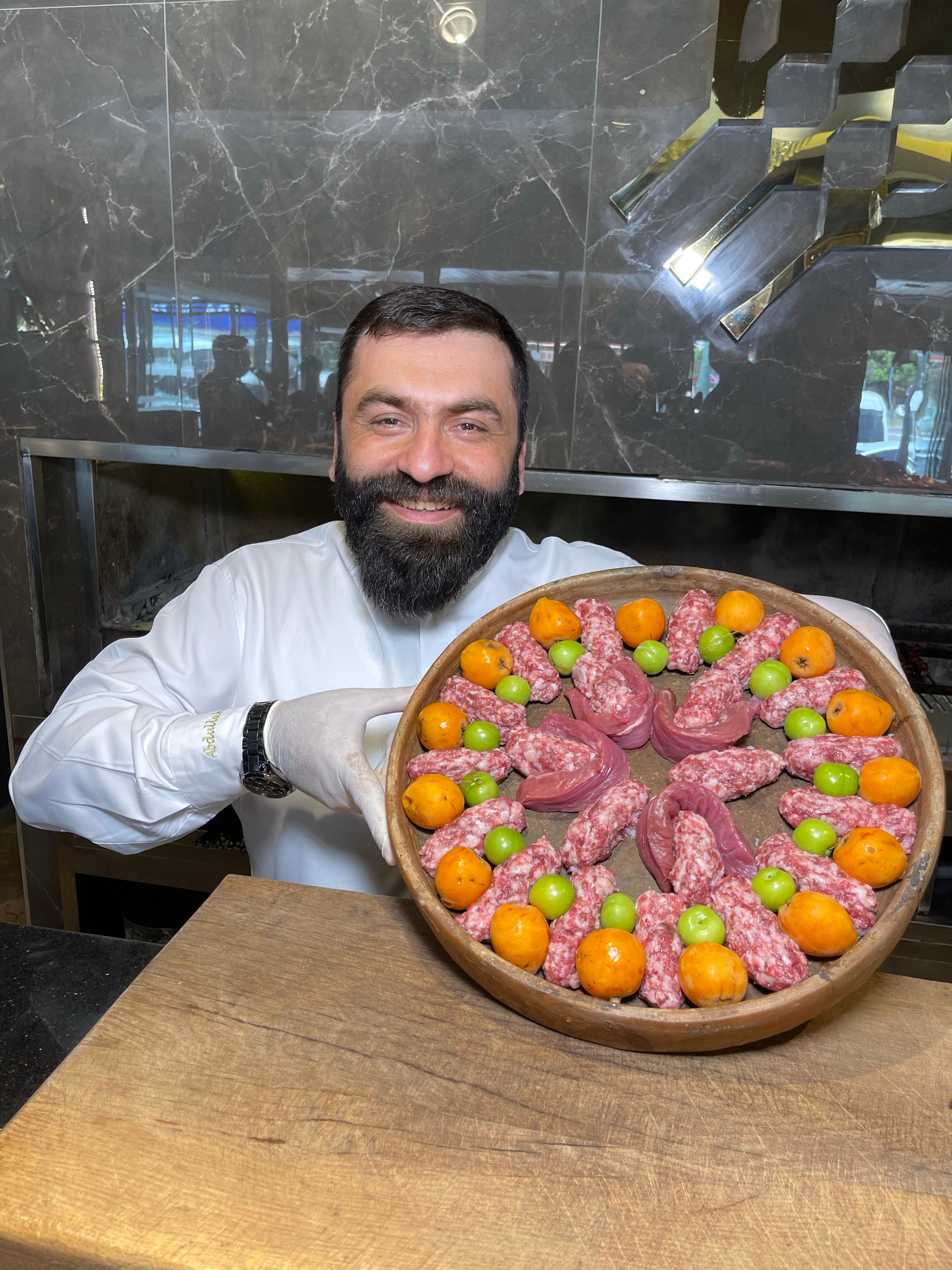 Bearded chef presenting an artisanal meat platter with vibrant colors indoors.