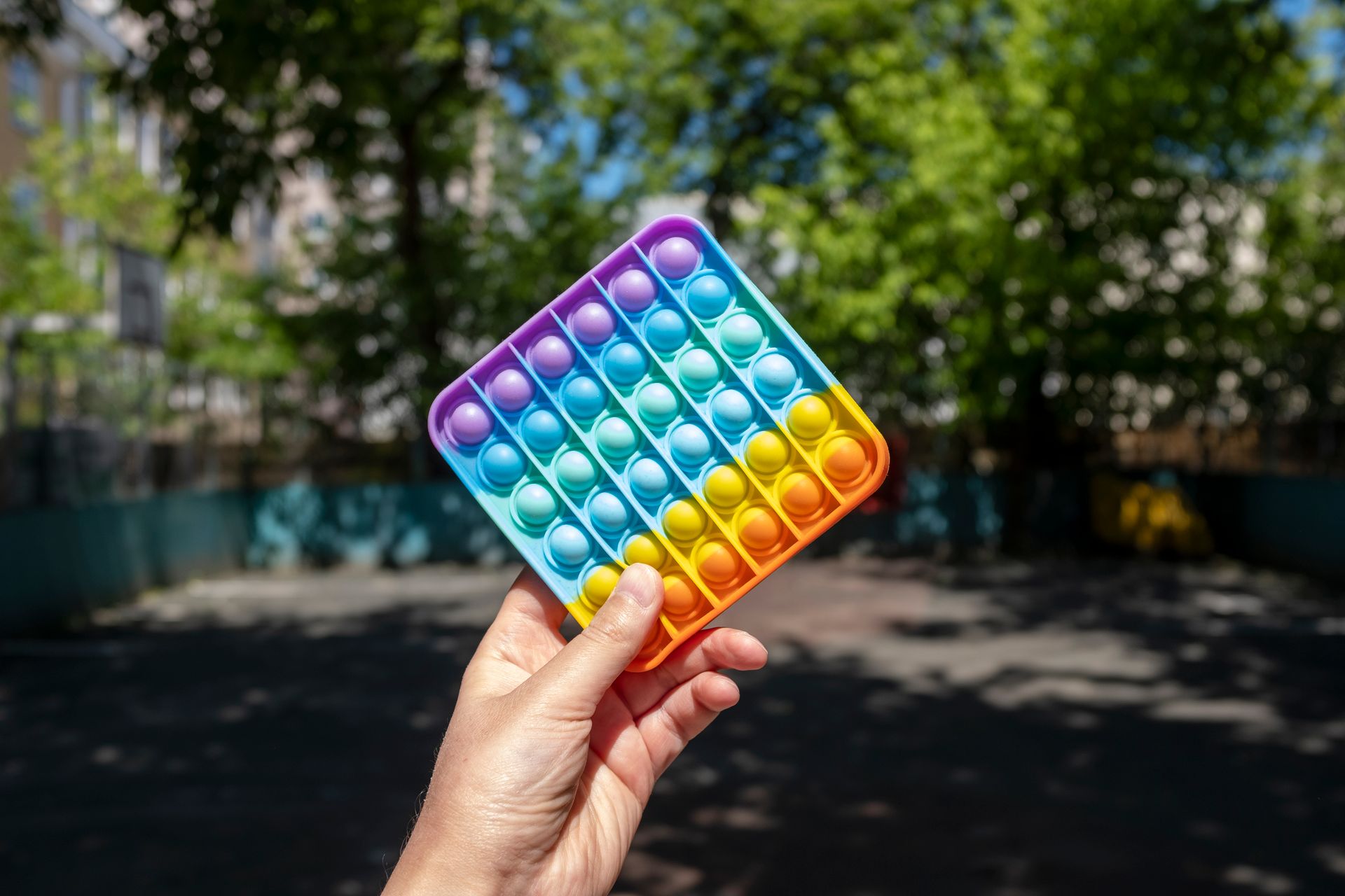 Vibrant rainbow Pop It toy held in hand with blurred outdoor background.