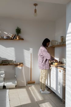 A person in a pink jacket prepares food in a bright, minimalist kitchen.