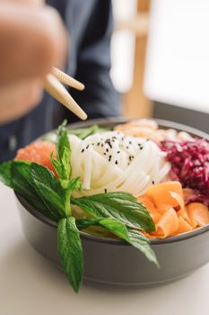 Tasty Asian noodle bowl with fresh vegetables and herbs, captured in close-up with chopsticks.