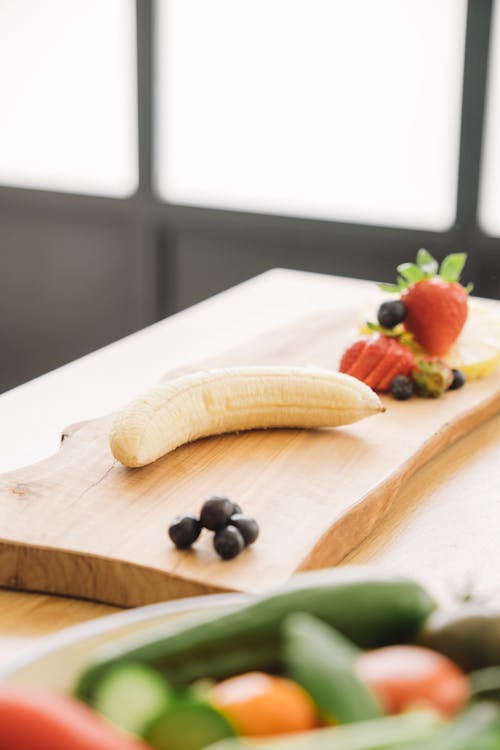 A Peeled Banana and Strawberry on a Wooden Chopping Board