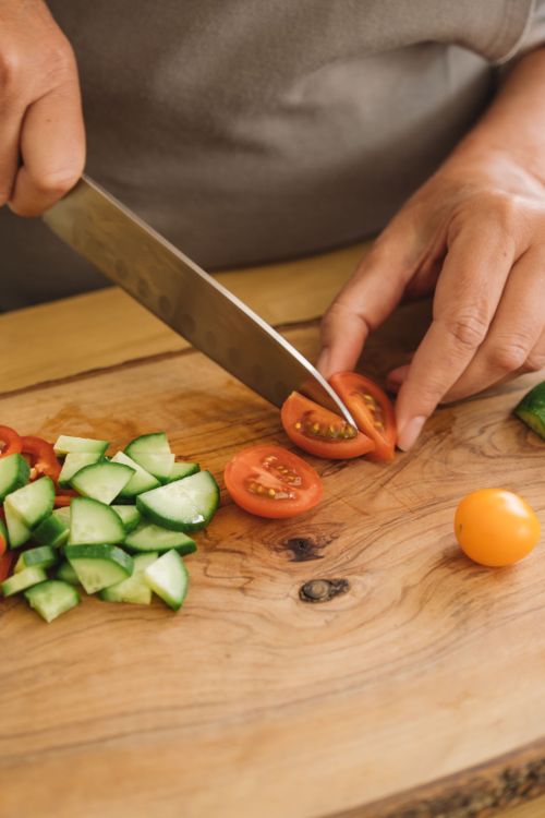 Free Close-up of hands slicing tomatoes and cucumbers on a wooden chopping board. Stock Photo