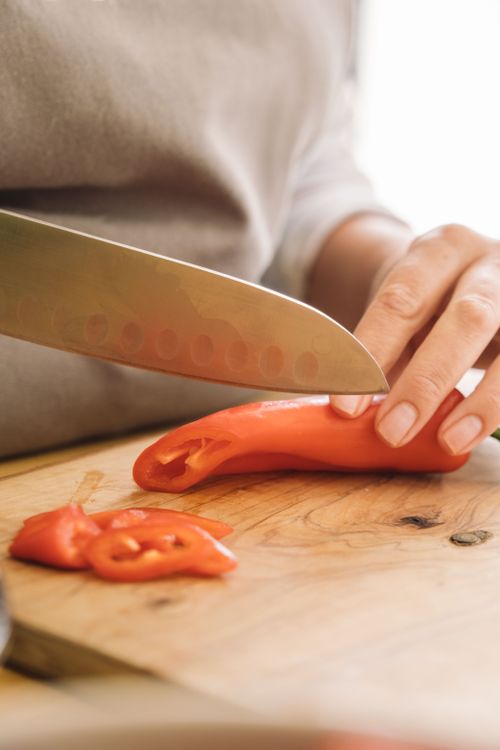 Free A hand slicing a fresh red pepper on a wooden chopping board with a sharp knife. Stock Photo