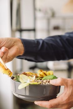 A person holding a bowl of healthy food with chopsticks, featuring a floral garnish.