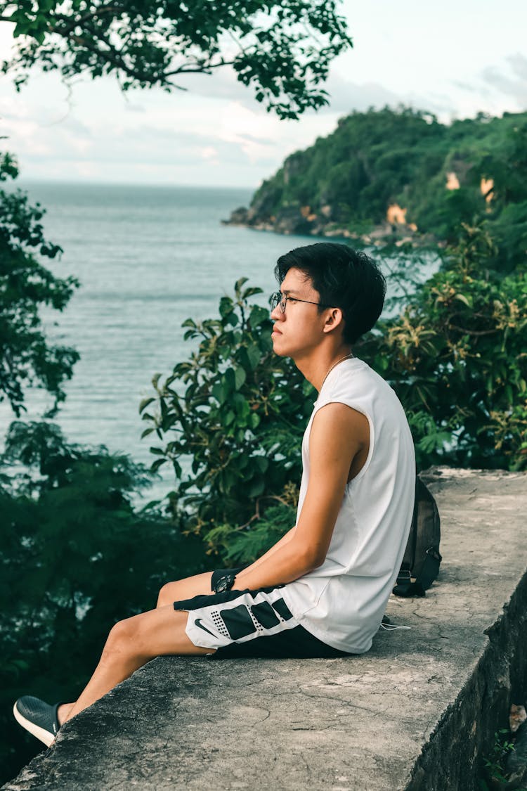 A Man In White Tank Top Sitting On A Concrete Bench While Looking At The View