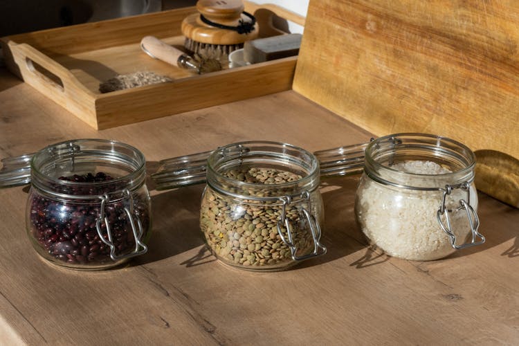 Clear Glass Jars With Raw Beans, Seeds And Rice On Brown Wooden Table