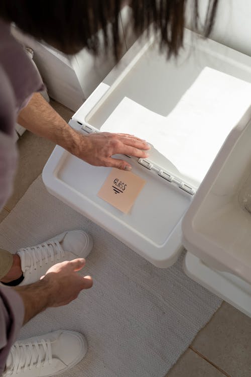 A Person Putting a Sticky Note on the White Trash Bin