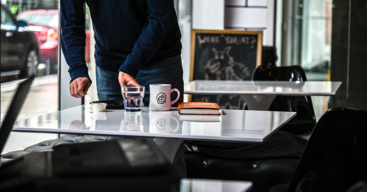 Uma pessoa organizando uma mesa de café com um livro, café e vidro em ambiente interno.