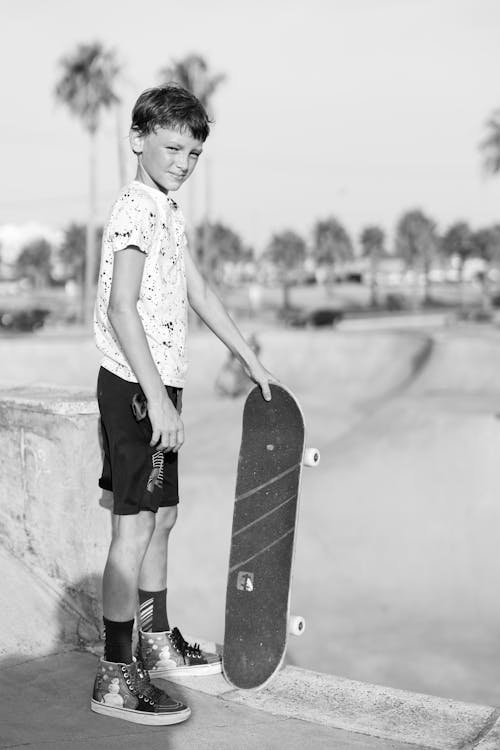 Grayscale Photo of a Boy Holding a Skateboard
