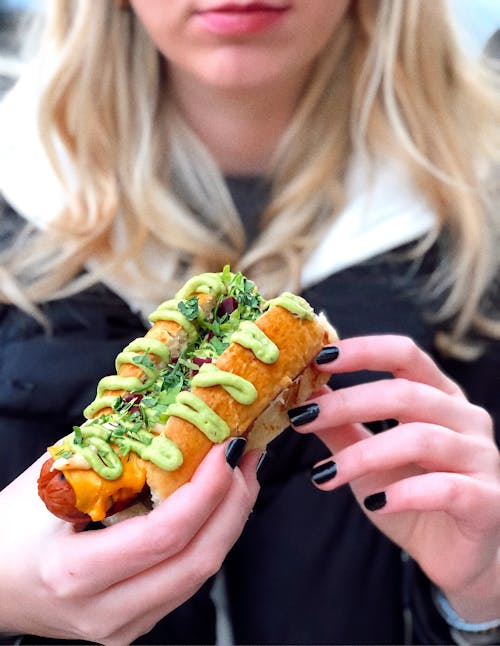 Close-Up Photo of a Woman with Black Manicured Fingernails Holding a Delicious Hot Dog Sandwich