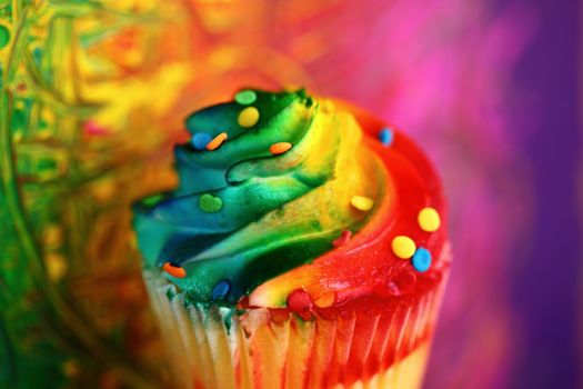 Close-up of a vibrant rainbow cupcake with colorful frosting and sprinkles.
