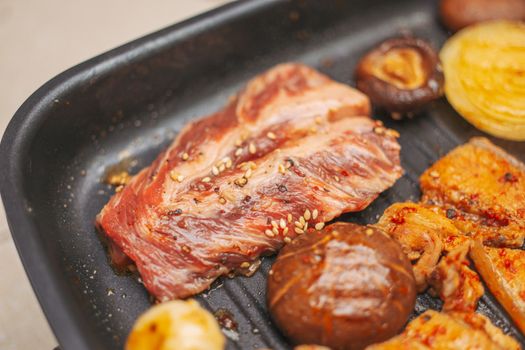 Close-up of marinated meat and vegetables grilling with sesame seeds, mushrooms, and onions.
