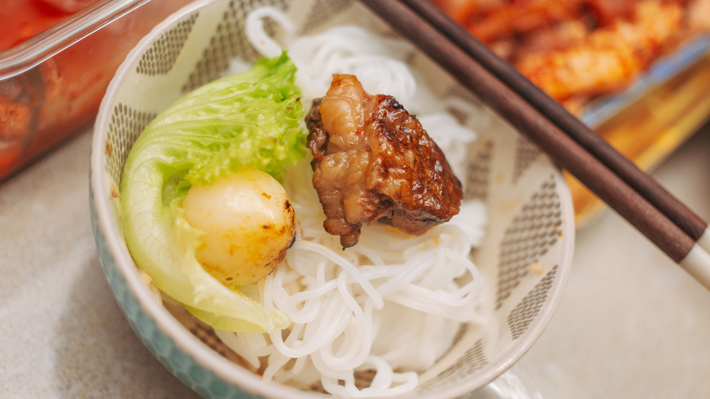 Delicious Asian dish featuring grilled meat, fresh lettuce, and noodles elegantly plated with chopsticks.