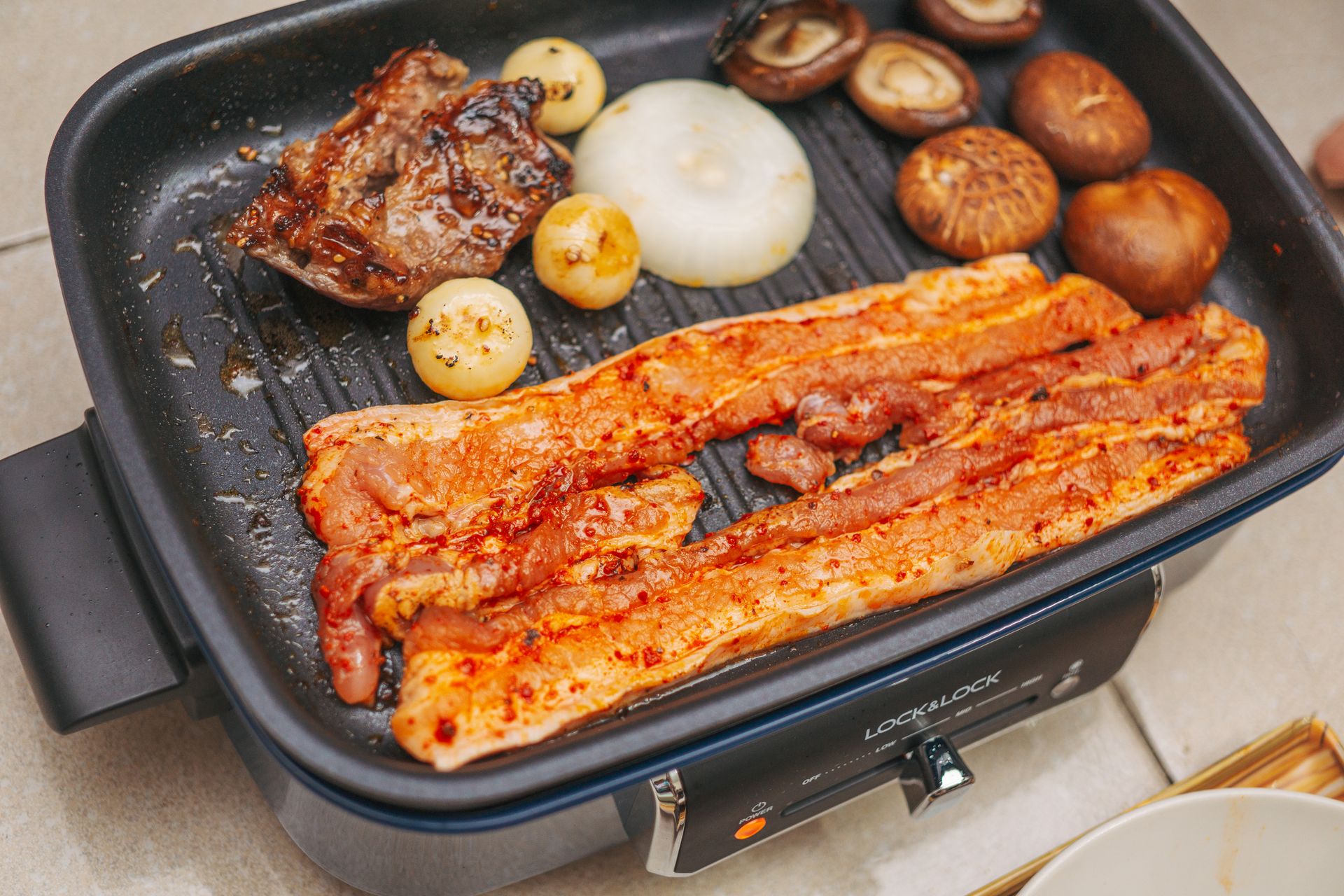 Strips of Pork and a Piece of Chicken on Electric Griller with Onions and Mushrooms