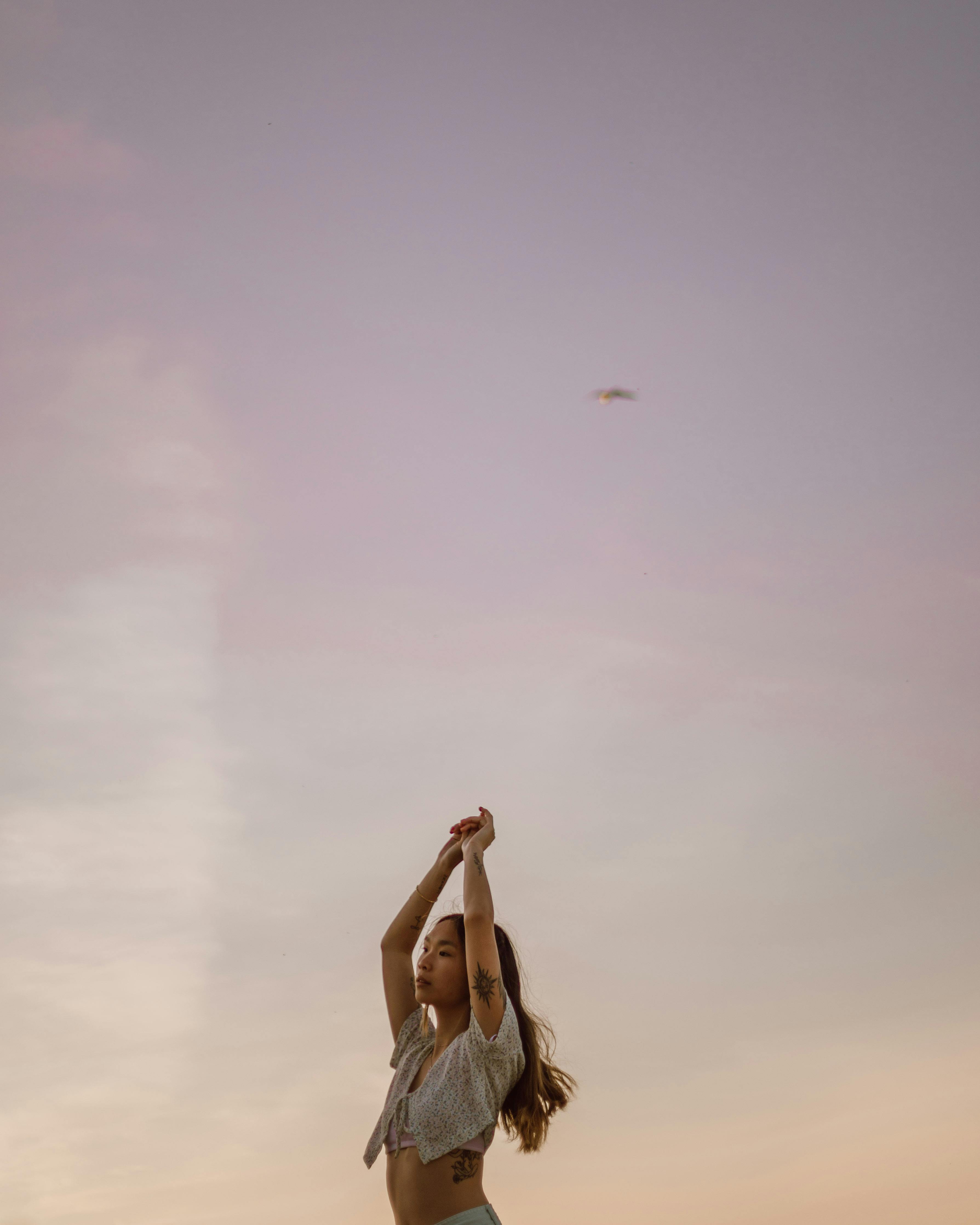 A woman with tattoos raises her arms against a colorful twilight sky, embodying freedom and expression.