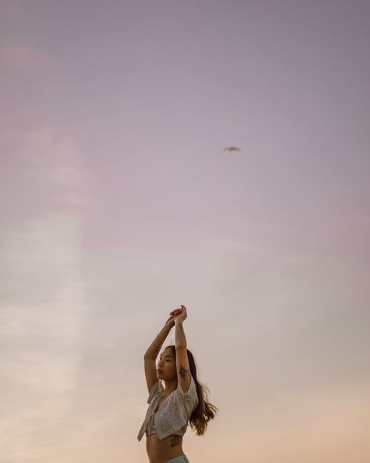 A woman with tattoos raises her arms against a colorful twilight sky, embodying freedom and expression.