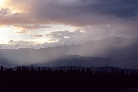 A stunning view of mountains with dramatic clouds and sunrays creating a mystical atmosphere.