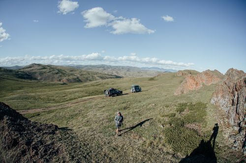 Free Breathtaking mountain landscape with off-road vehicles and a lone explorer, capturing the essence of adventure. Stock Photo