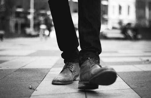 Grayscale Photo of a Person Walking in Formal Shoes