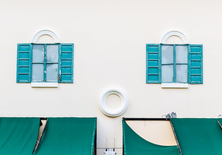 A White Concrete Building With Blue Window Shutters And Green Canopies