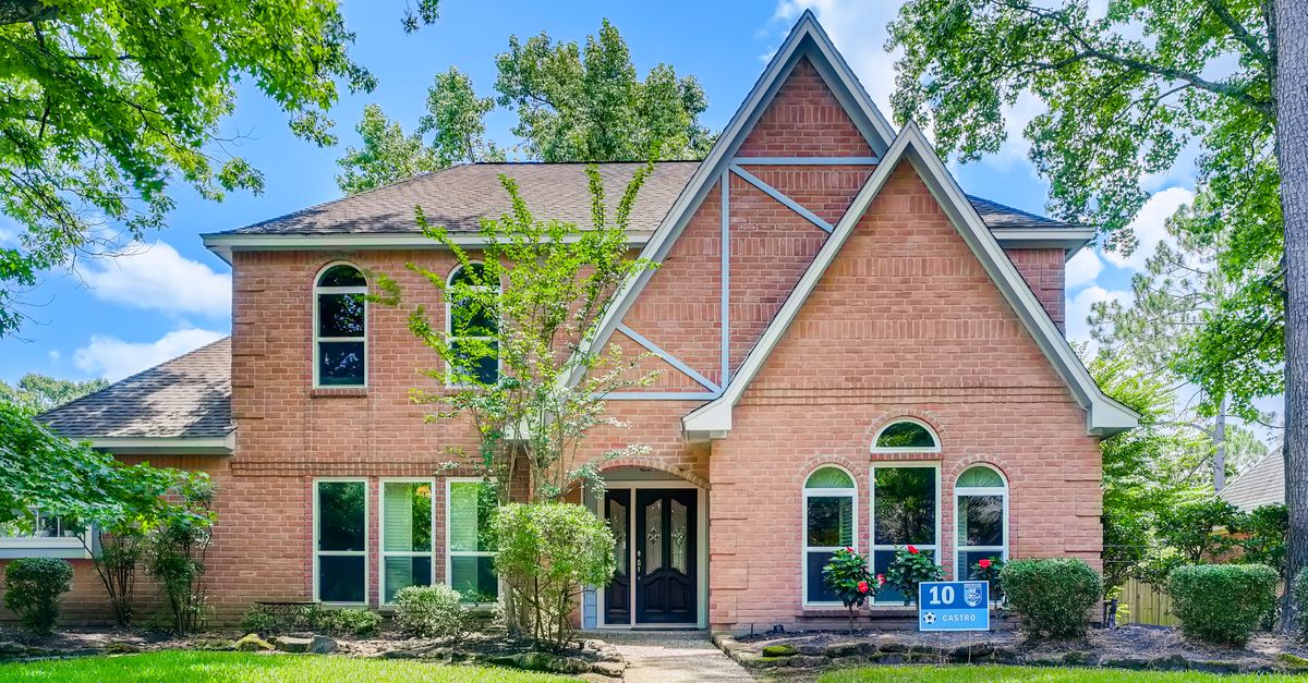 Two-story brick house with lush front yard, trees, and striking architecture.