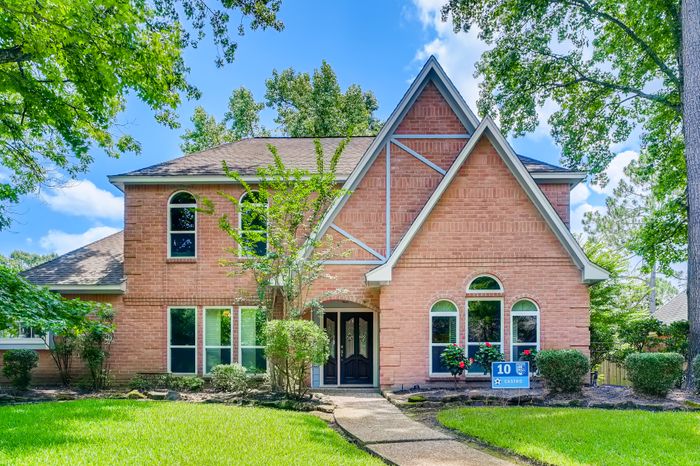 Two-story brick home with a landscaped front yard, listed for sale in a leafy suburb