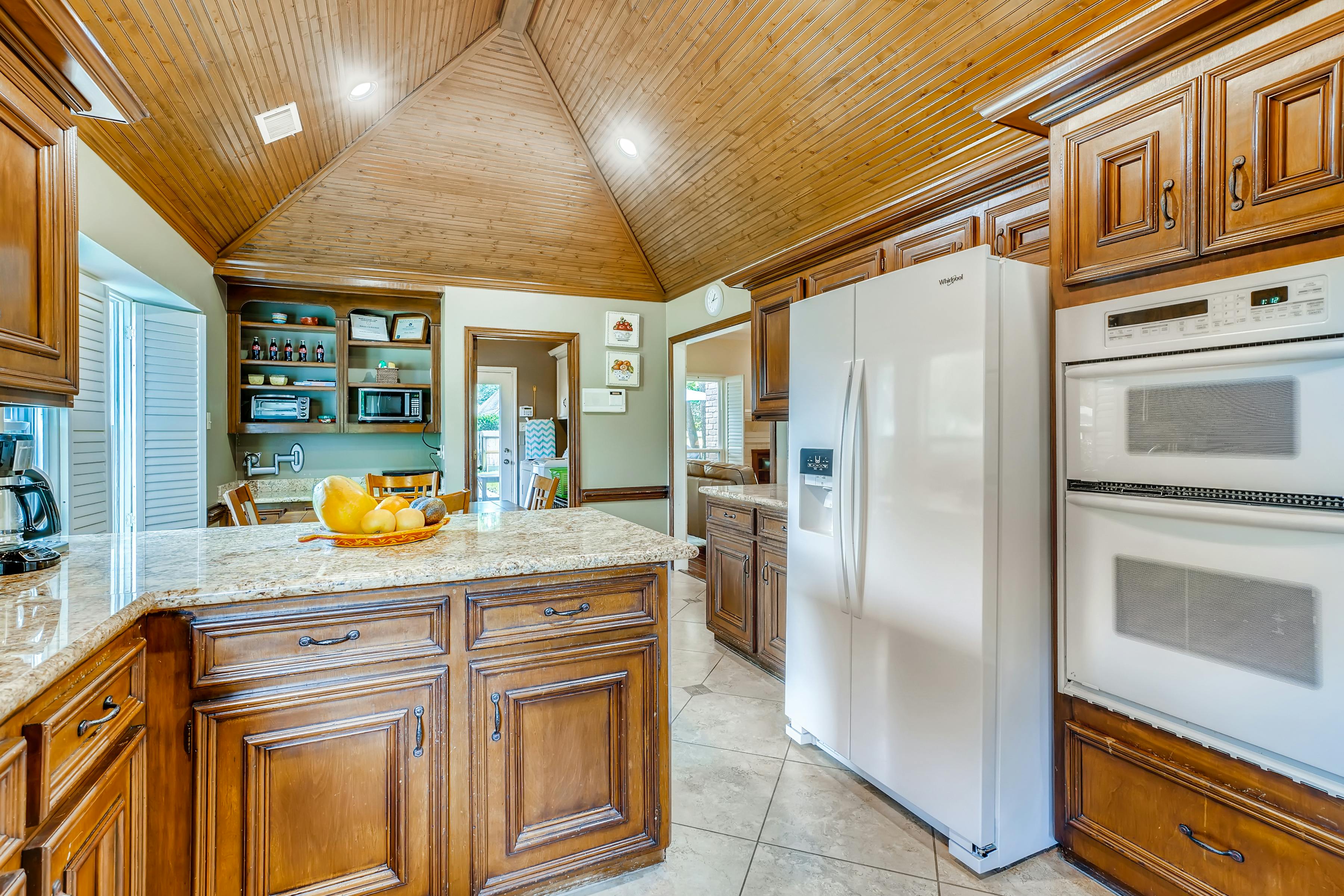 Spacious wooden kitchen interior featuring granite countertop, refrigerator, and built-in appliances with abundant natural light.