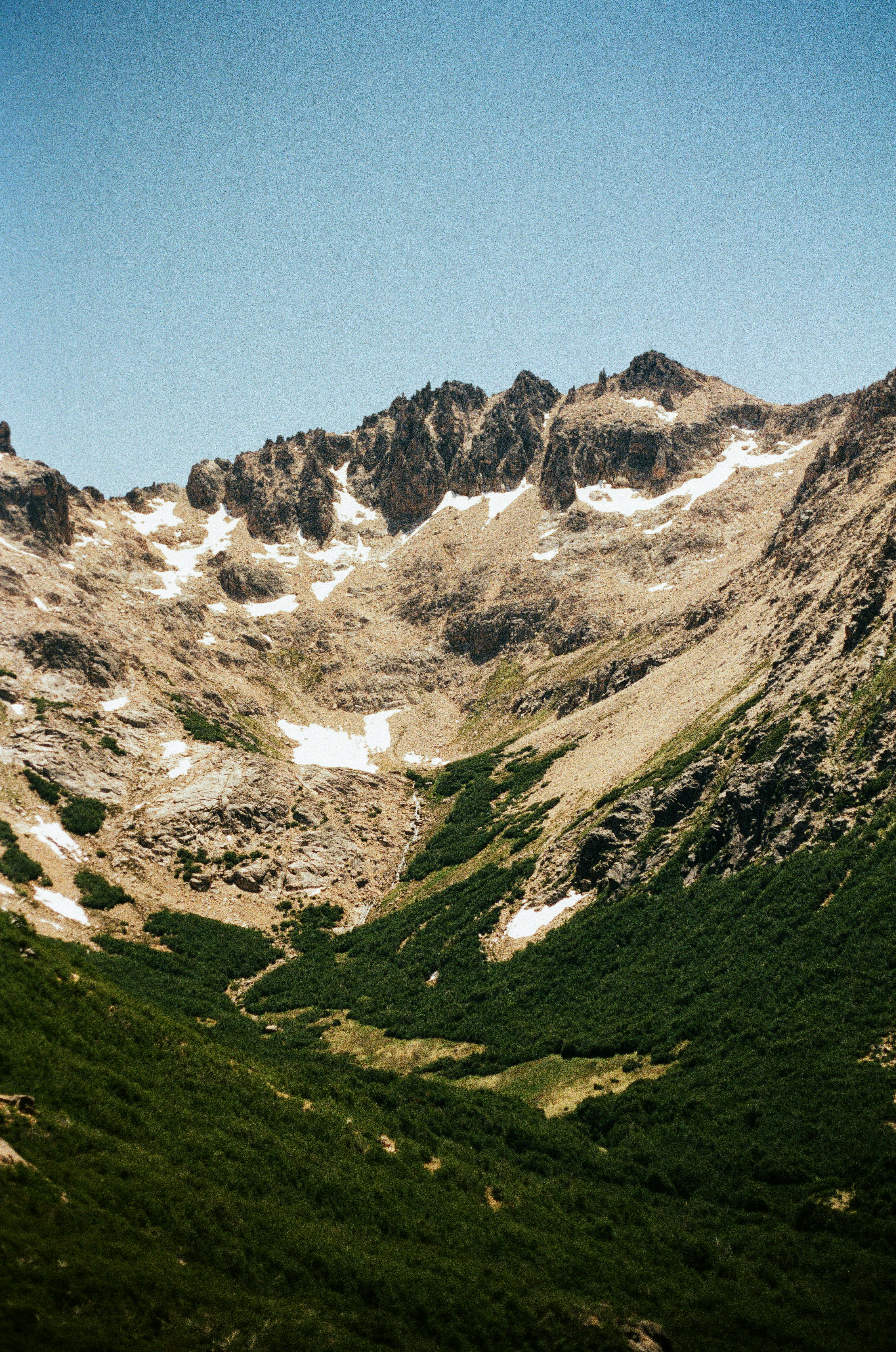 Breathtaking view of a rugged mountain with snow patches against a clear blue sky.