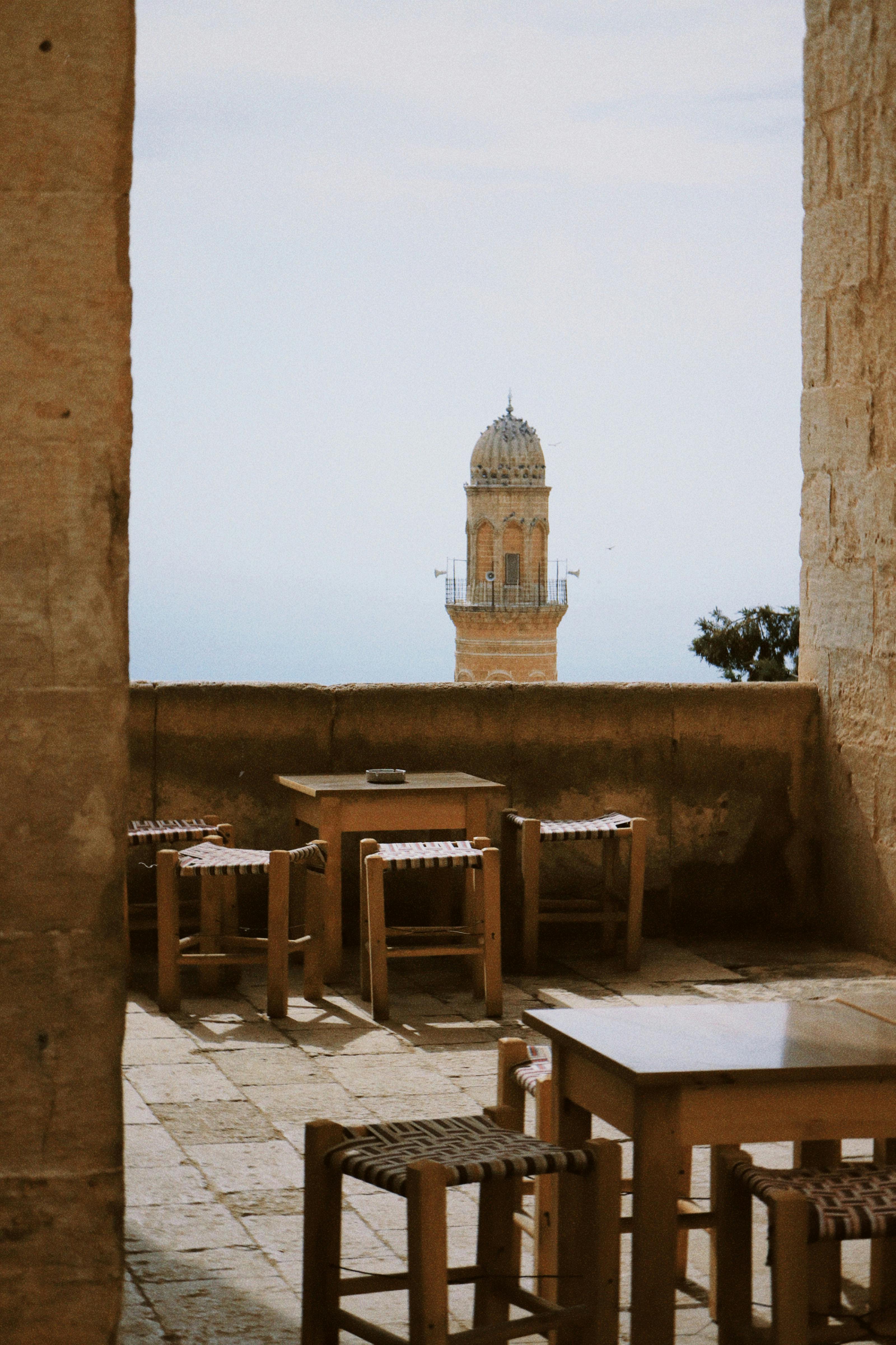 Rustic stone terrace with tables and view of historic minaret in Mardin, Türkiye.