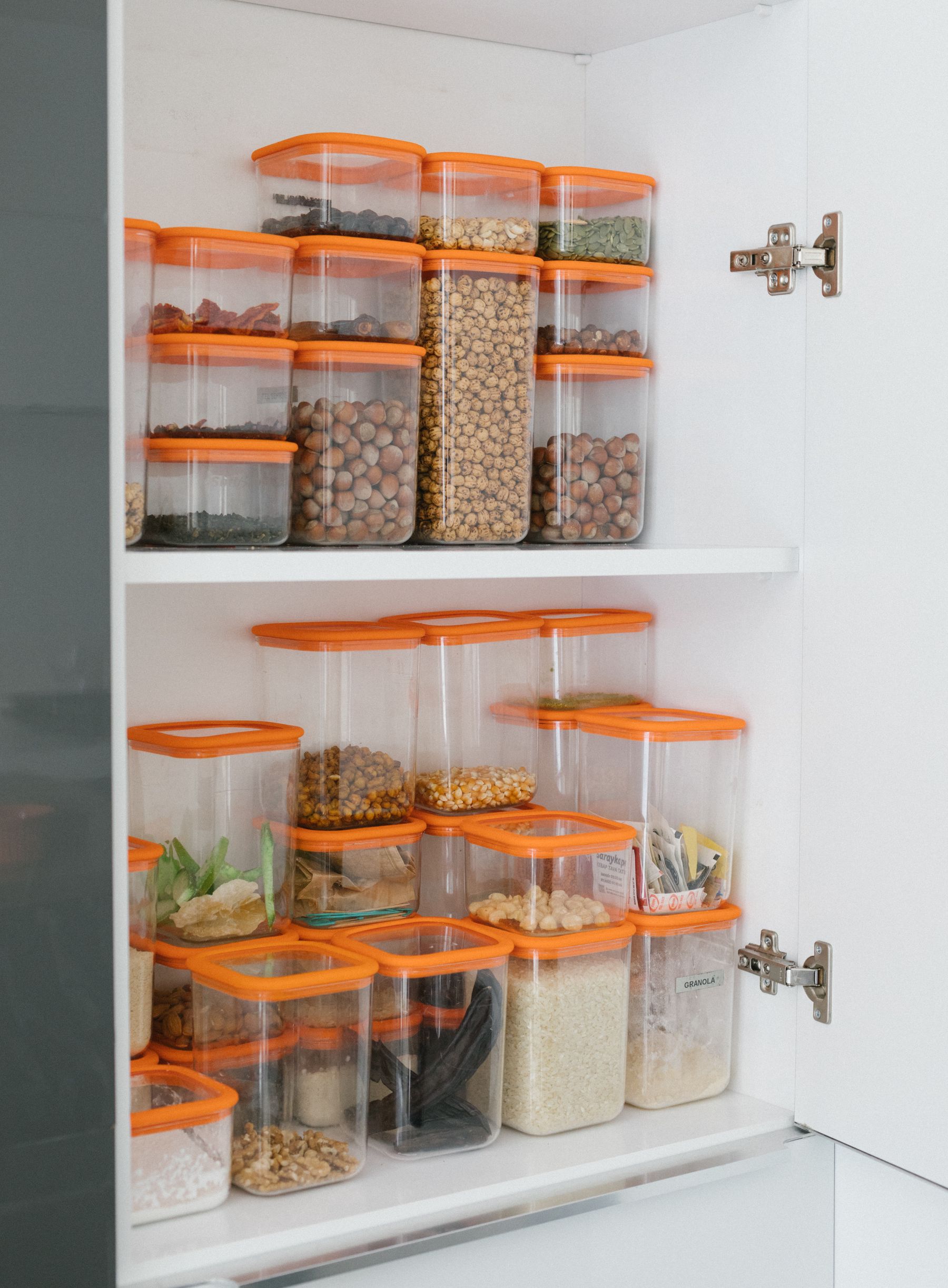 Clear pantry containers filled with grains, beans, nuts, and spices arranged on a white storage shelf