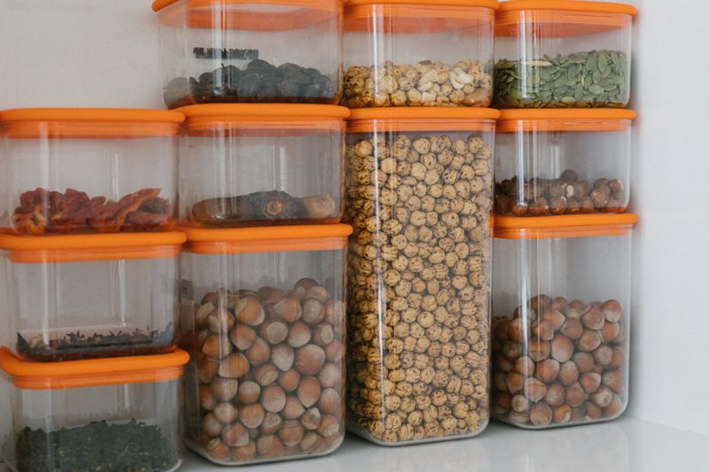 Various nuts and grains stored in transparent plastic containers with orange lids, organized neatly.