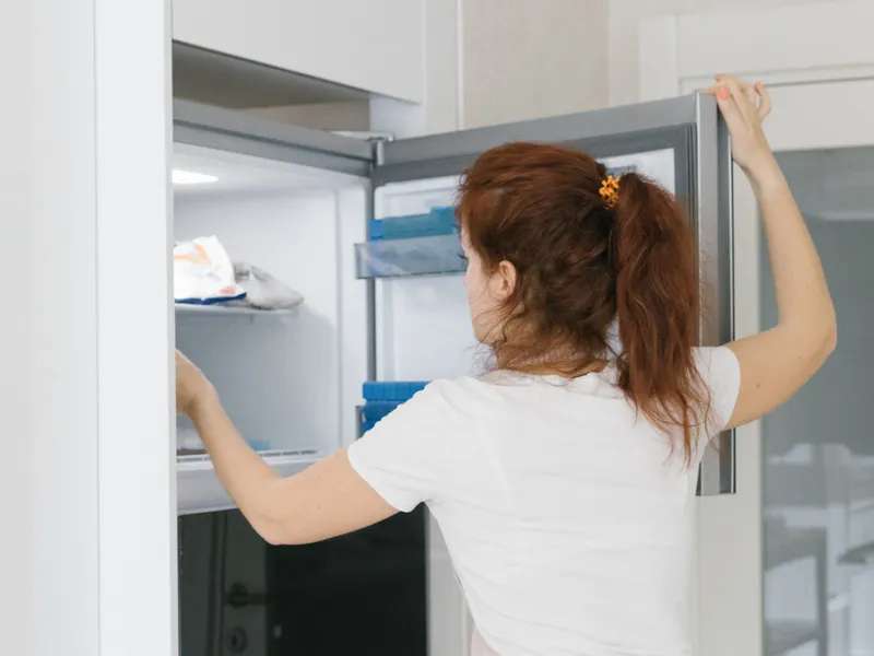 Woman opening a refrigerator door in a modern kitchen to check the door gasket seal Woman opening a refrigerator door in a modern kitchen to check the door gasket seal