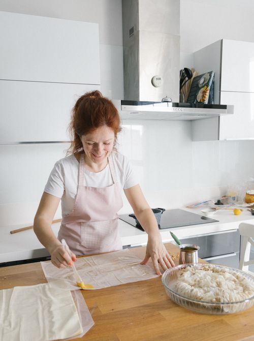 Free Smiling woman in an apron prepares pastry on a wooden table in a stylish Istanbul kitchen. Stock Photo
