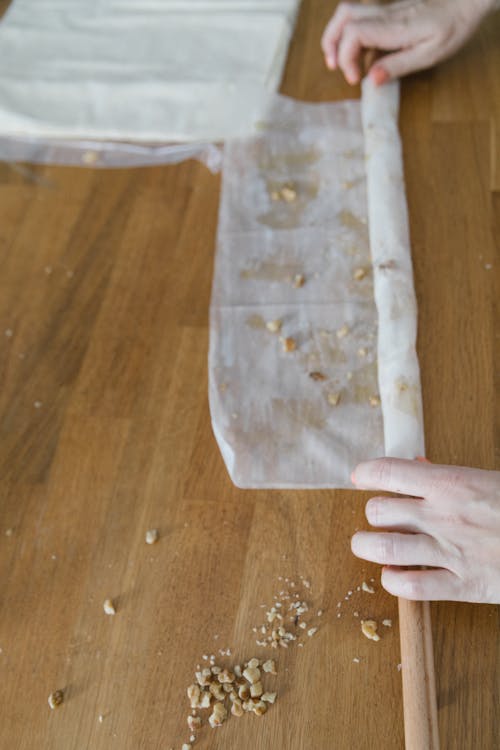 A Person Rolling a Thin Dough with Crushed Nuts