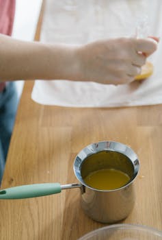 A person squeezing lemon over a saucepan with fresh juice, on a wooden table.