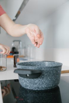 Hand adding cloves to a casserole dish on a modern kitchen cooktop.