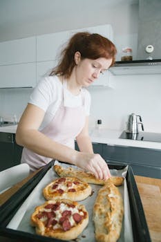 Woman preparing homemade Turkish pide in a modern kitchen, adding toppings to flatbread.