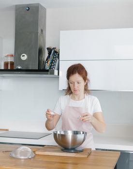 Woman in a modern kitchen preparing food, using a mixing bowl on a wooden countertop.
