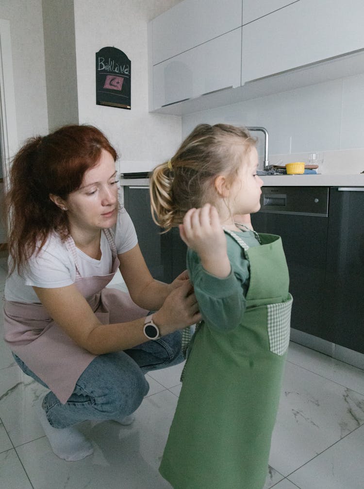 A Woman Tying The Apron Of Her Daughter