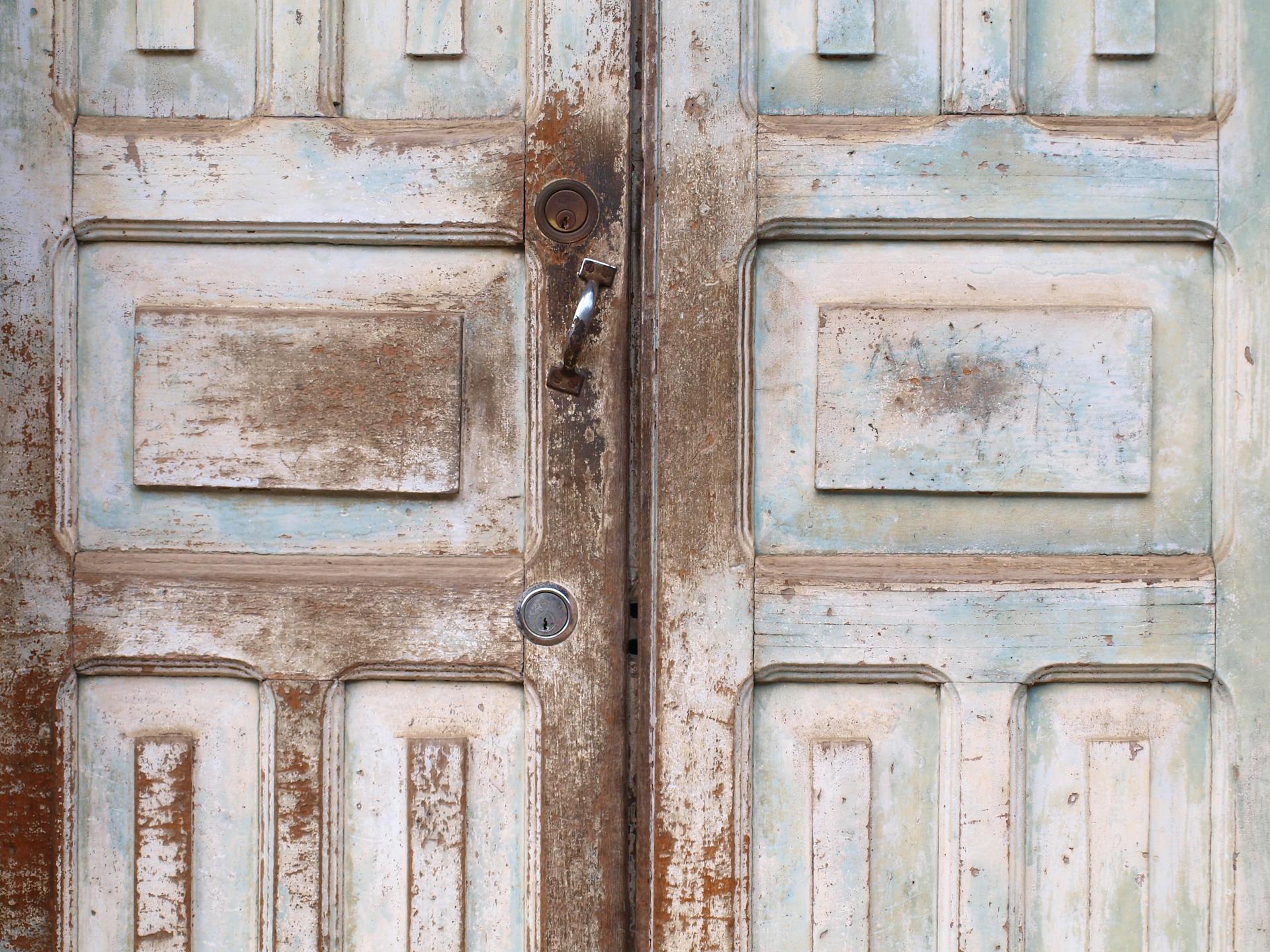 Close-up of rustic vintage wooden double doors with antique hardware and textured finish.
