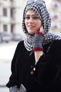 Portrait of a smiling woman wearing a checkered headscarf and winter gloves outdoors.